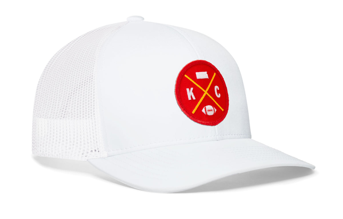 white trucker hat viewed from the right side, showcasing a bold red and gold embroidered X patch prominently displayed on the front