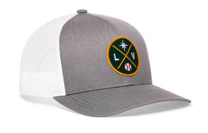 gray-white trucker hat viewed from the right side, showcasing a bold green and gold embroidered X patch prominently displayed on the front