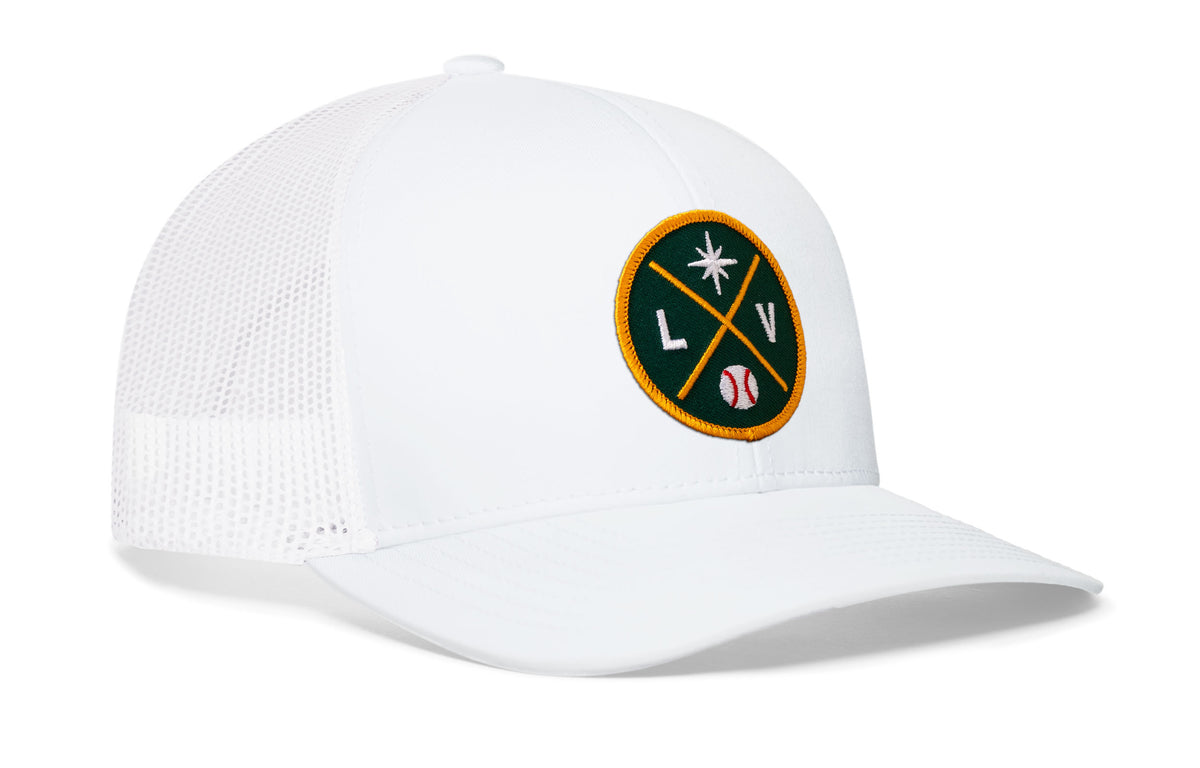 white trucker hat viewed from the right side, showcasing a bold green and gold embroidered X patch prominently displayed on the front