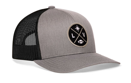 gray-black trucker hat viewed from the right side, showcasing a bold silver and black embroidered X patch prominently displayed on the front