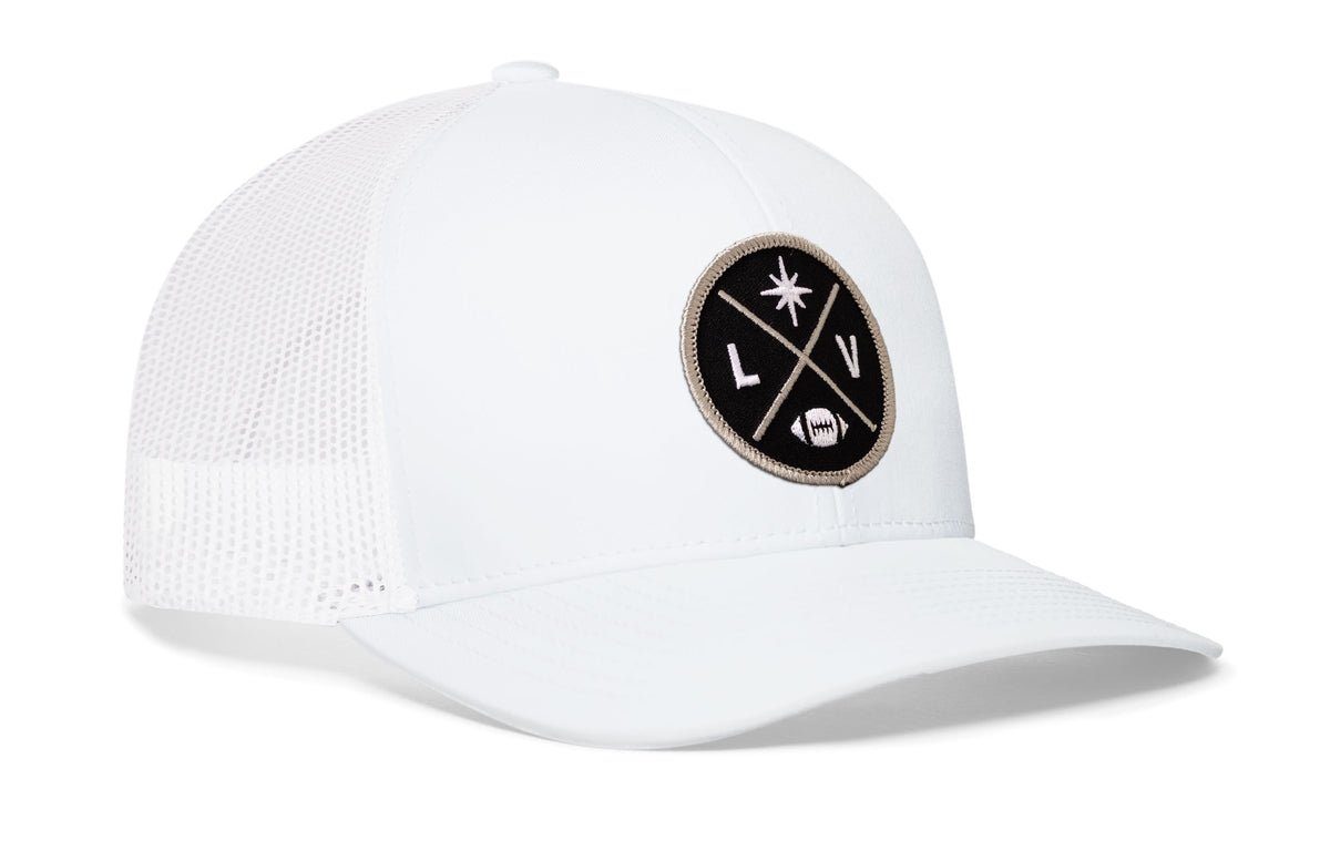 white trucker hat viewed from the right side, showcasing a bold silver and black embroidered X patch prominently displayed on the front