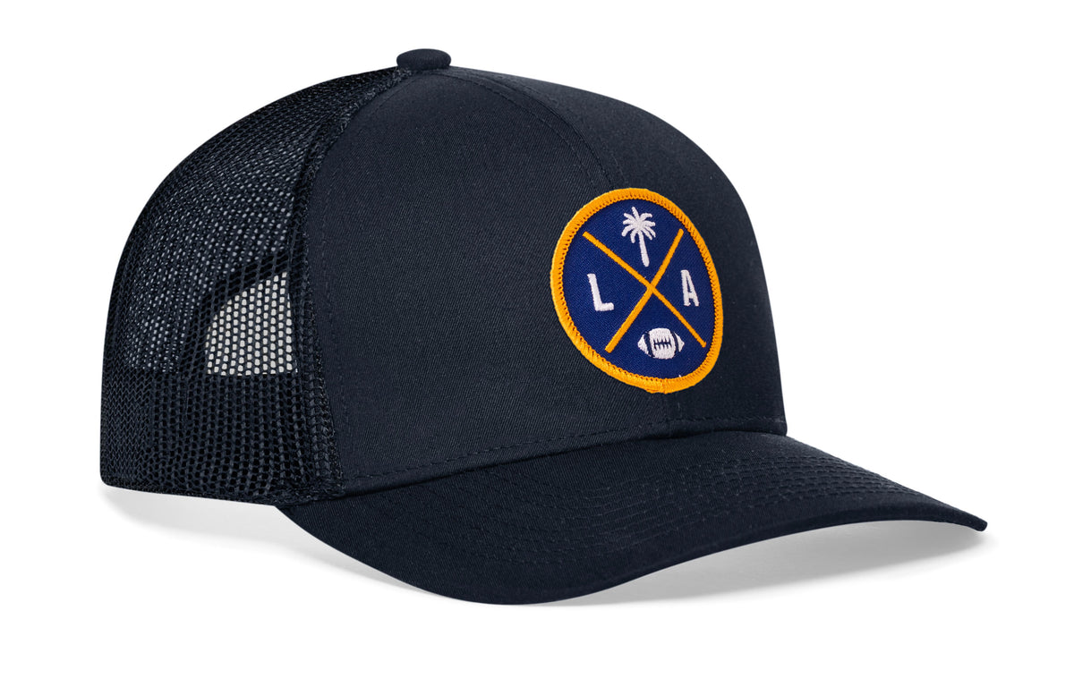 navy trucker hat viewed from the right side, showcasing a bold dark blue and yellow embroidered X patch prominently displayed on the front