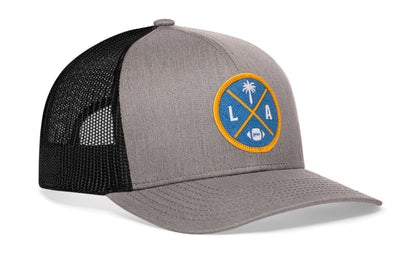 gray-black trucker hat viewed from the right side, showcasing a bold light blue and yellow embroidered X patch prominently displayed on the front