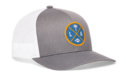 gray-white trucker hat viewed from the right side, showcasing a bold light blue and yellow embroidered X patch prominently displayed on the front