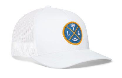 white trucker hat viewed from the right side, showcasing a bold light blue and yellow embroidered X patch prominently displayed on the front