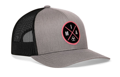 gray-black trucker hat viewed from the right side, showcasing a bold black and pink embroidered X patch prominently displayed on the front