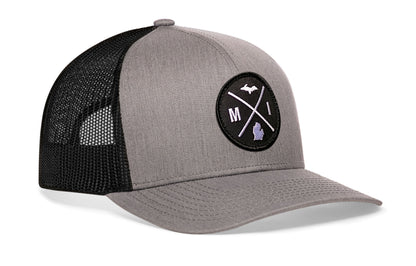 gray-black trucker hat viewed from the right side, showcasing a bold black and white embroidered X patch prominently displayed on the front