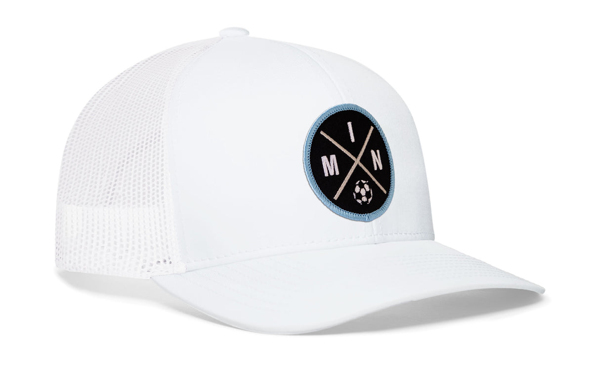 white trucker hat viewed from the right side, showcasing a bold black and blue embroidered X patch prominently displayed on the front