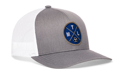 gray-white trucker hat viewed from the right side, showcasing a bold blue and black embroidered X patch prominently displayed on the front