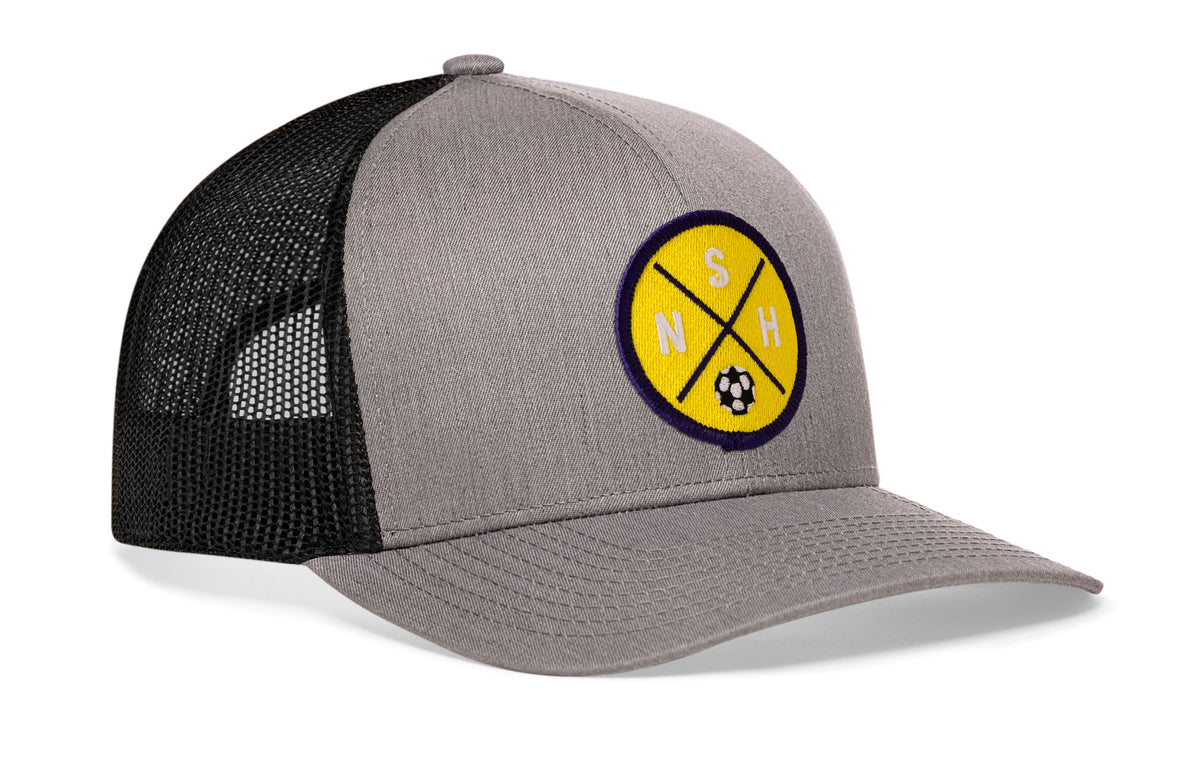gray-black trucker hat viewed from the right side, showcasing a bold yellow and blue embroidered X patch prominently displayed on the front