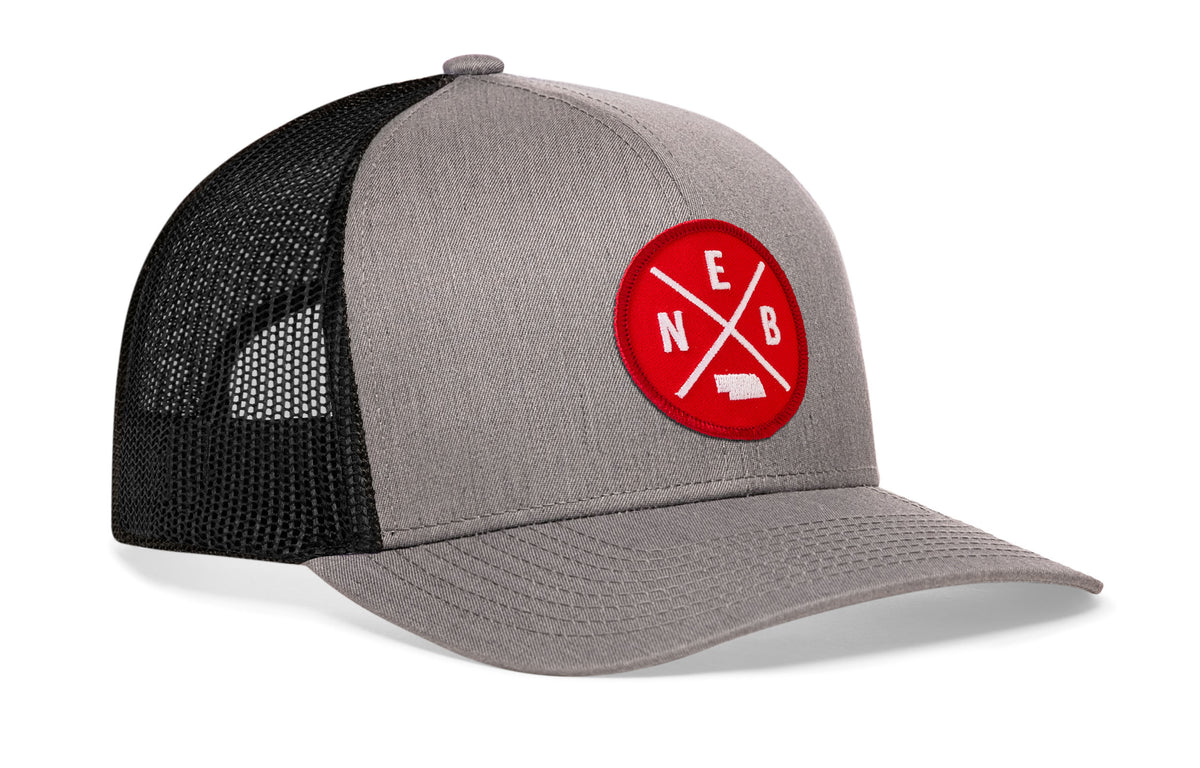 gray-black trucker hat viewed from the right side, showcasing a bold red and white embroidered patch prominently displayed on the front