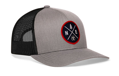 gray-black trucker hat viewed from the right side, showcasing a bold red and blue embroidered X patch prominently displayed on the front