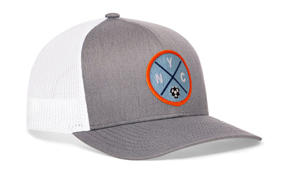 gray-white trucker hat viewed from the right side, showcasing a bold sky blue and orange embroidered X patch prominently displayed on the front