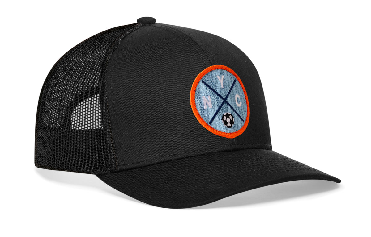 black trucker hat viewed from the right side, showcasing a bold sky blue and orange embroidered X patch prominently displayed on the front