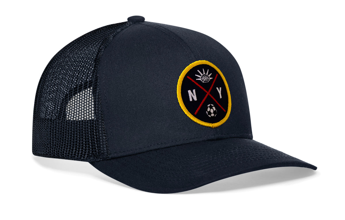 navy trucker hat viewed from the right side, showcasing a bold sky blue and orange embroidered X patch prominently displayed on the front