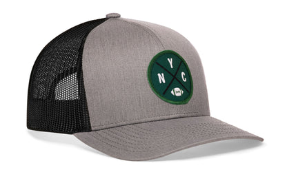 gray-black trucker hat viewed from the right side, showcasing a bold green, white and black embroidered X patch prominently displayed on the front