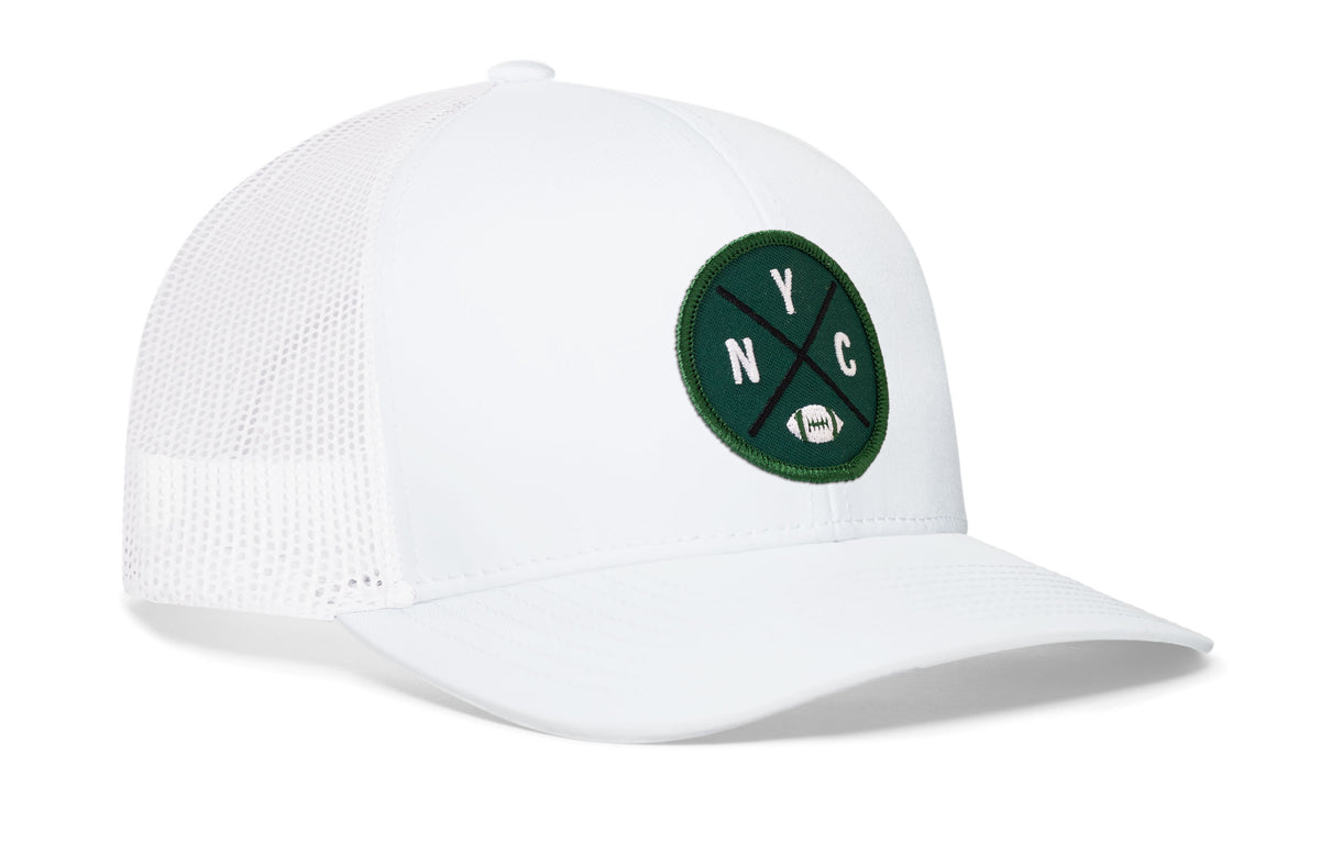 white trucker hat viewed from the right side, showcasing a bold green, white and black embroidered X patch prominently displayed on the front