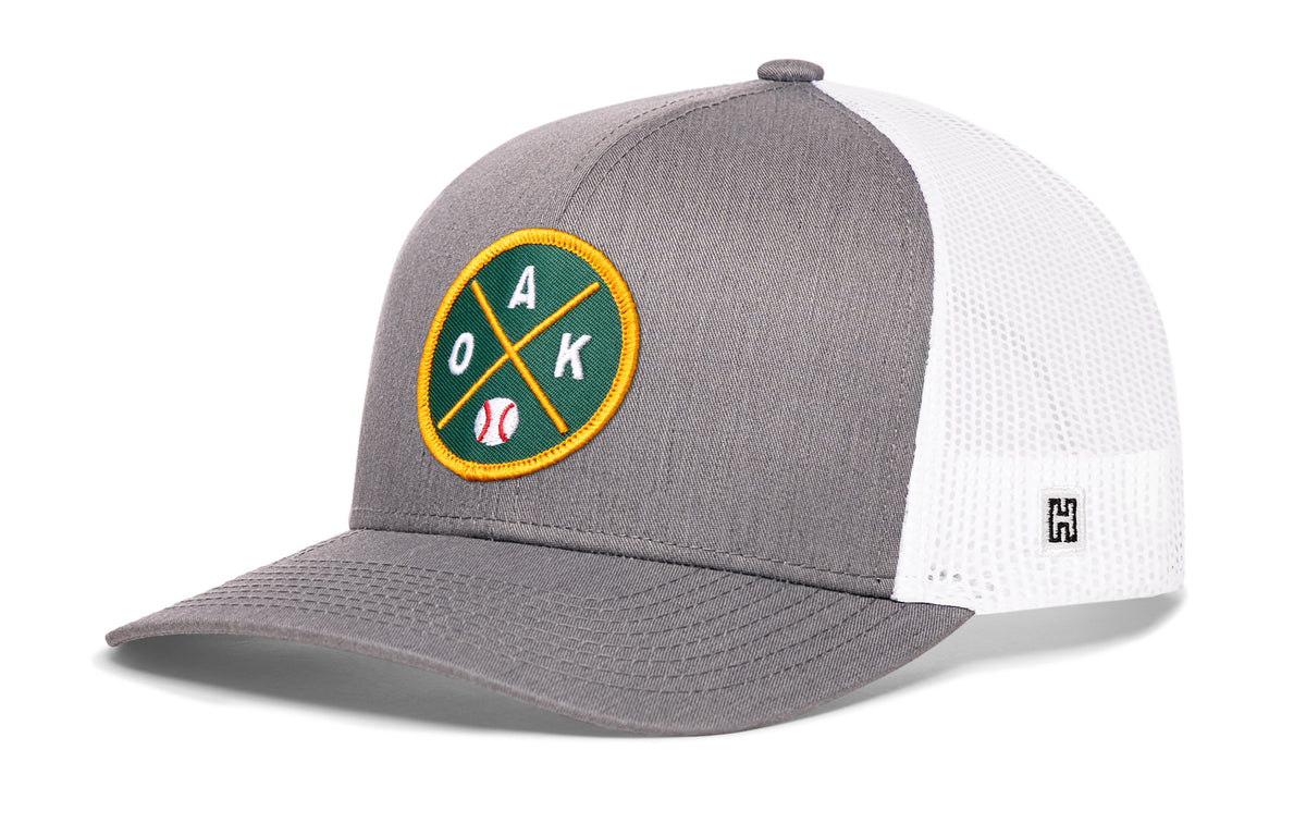 Oakland Baseball Trucker Hat, gray-white snapback showing Haka brandmark on left side of cap.