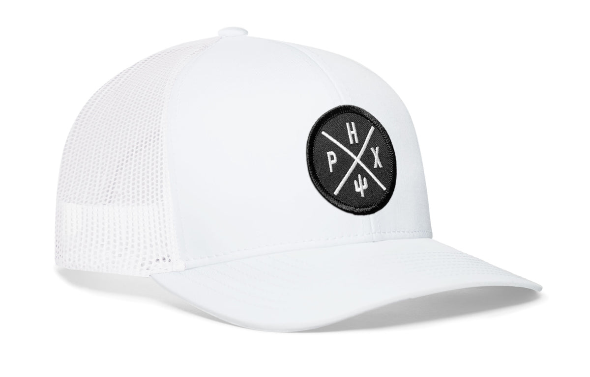 white trucker hat viewed from the right side, showcasing a bold black and white embroidered X patch prominently displayed on the front