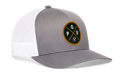 gray-white trucker hat viewed from the right side, showcasing a bold forest green and gold embroidered X patch prominently displayed on the front