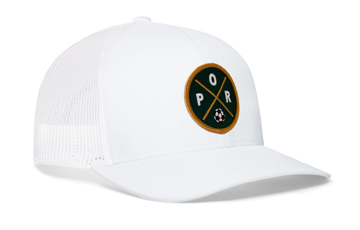 white trucker hat viewed from the right side, showcasing a bold forest green and gold embroidered X patch prominently displayed on the front