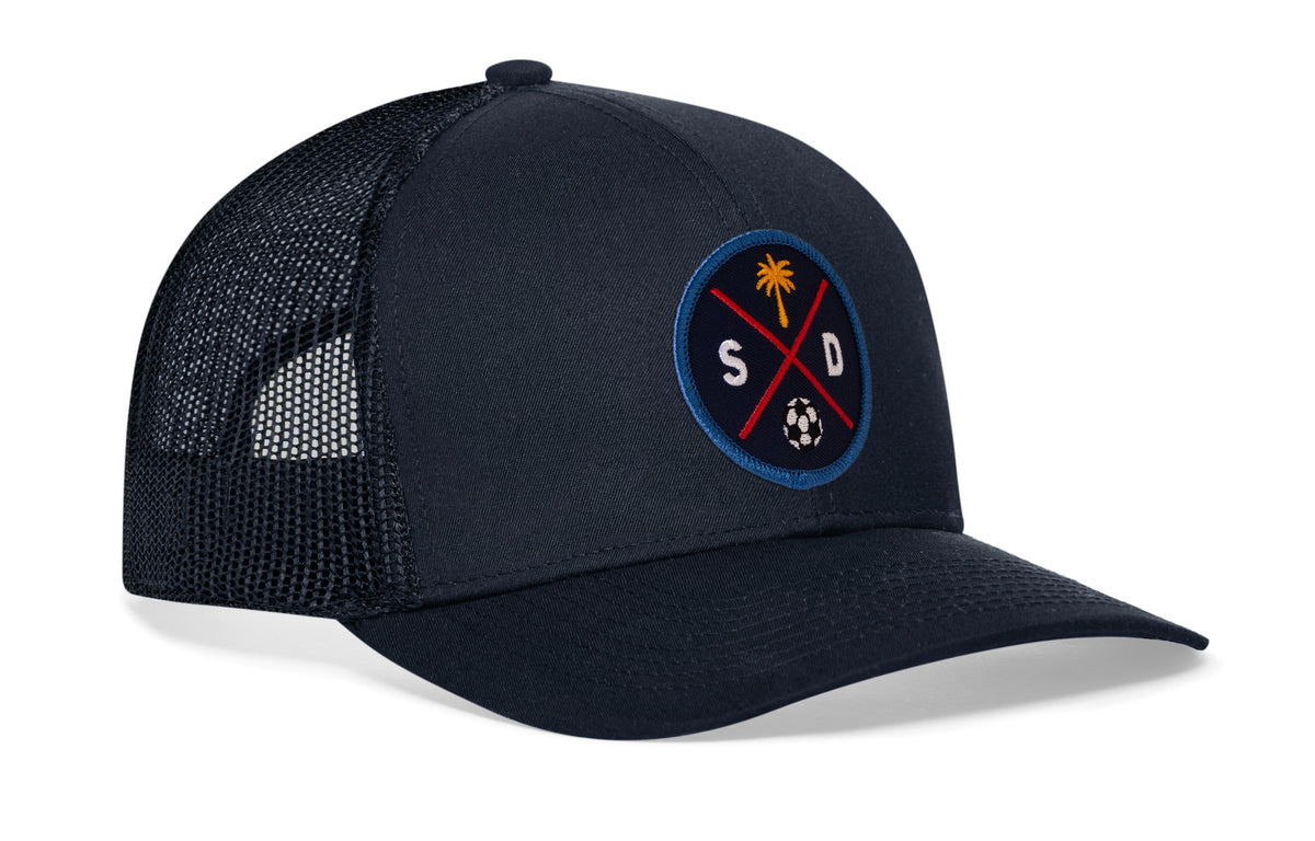 navy trucker hat viewed from the right side, showcasing a bold navy and orange embroidered X patch prominently displayed on the front