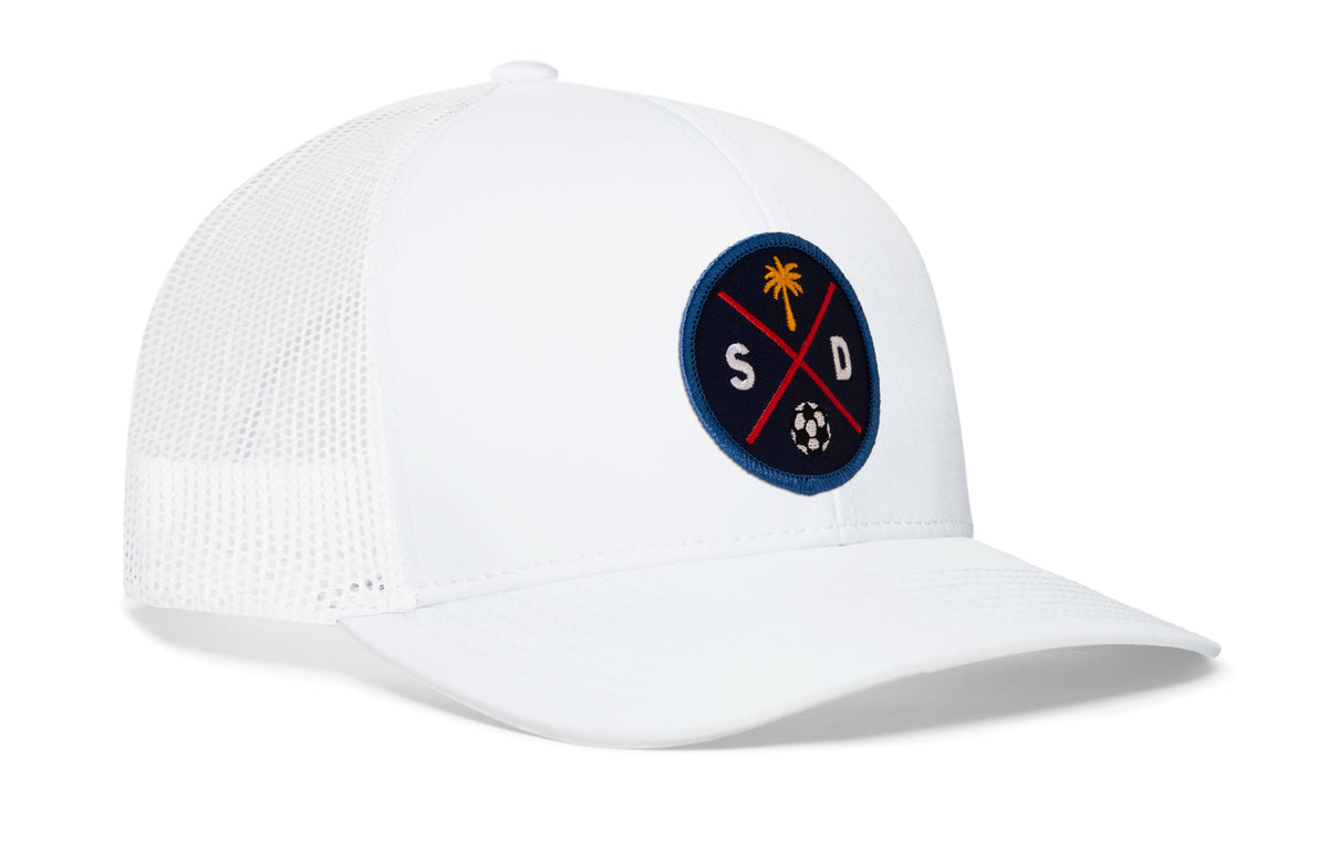 white trucker hat viewed from the right side, showcasing a bold navy and orange embroidered X patch prominently displayed on the front