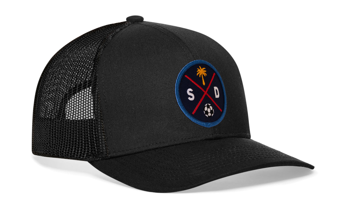 black trucker hat viewed from the right side, showcasing a bold navy and orange embroidered X patch prominently displayed on the front