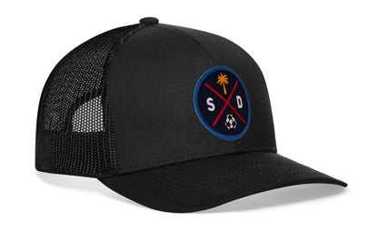 black trucker hat viewed from the right side, showcasing a bold navy and orange embroidered X patch prominently displayed on the front