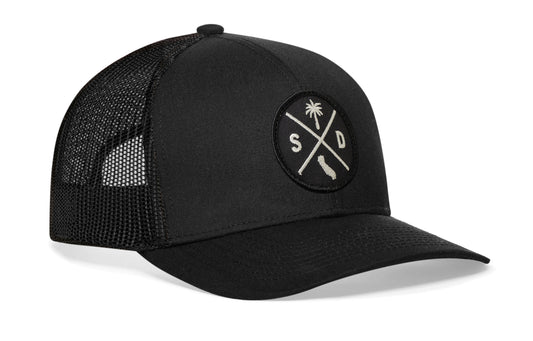 black trucker hat viewed from the right side, showcasing a bold black and white embroidered X patch prominently displayed on the front
