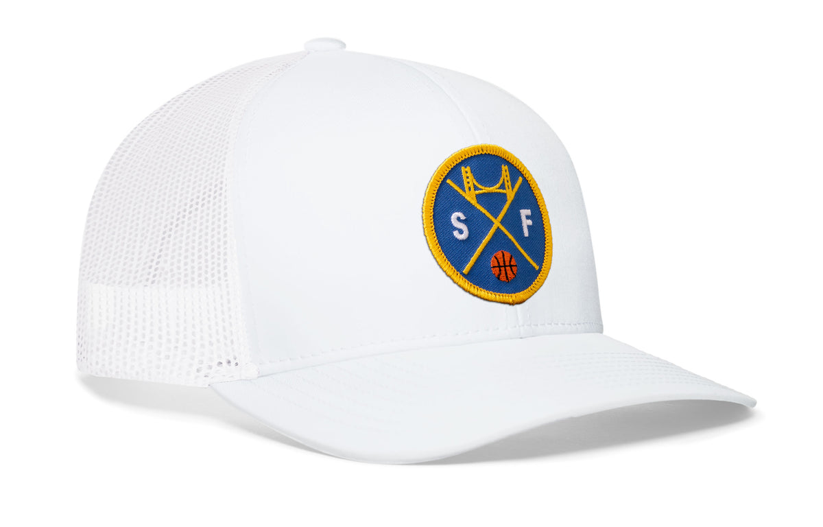 white trucker hat viewed from the right side, showcasing a bold royal blue and gold embroidered X patch prominently displayed on the front