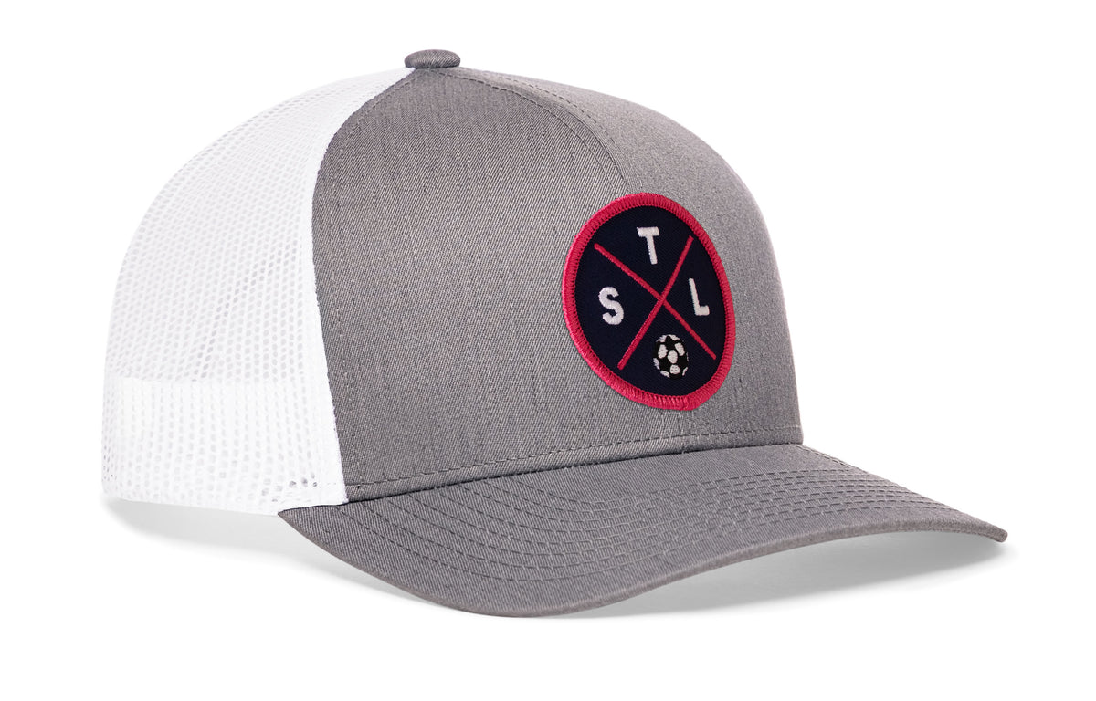 gray-white trucker hat viewed from the right side, showcasing a bold red and blue embroidered X patch prominently displayed on the front