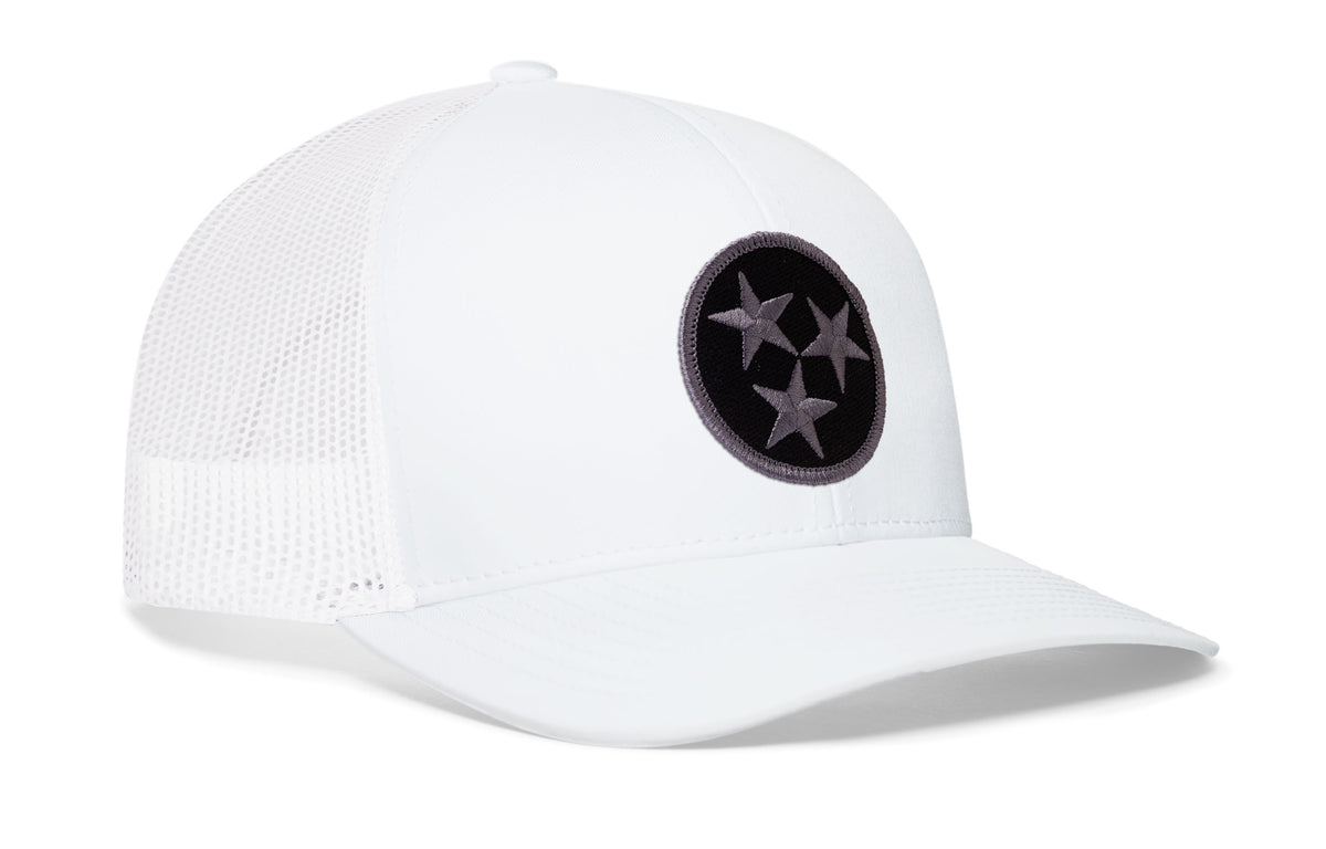 white trucker hat viewed from the right side, showcasing a bold black and gray embroidered flag patch prominently displayed on the front