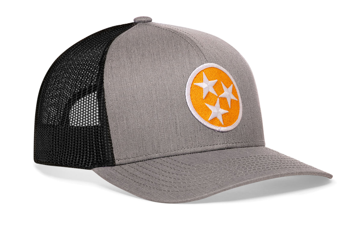 gray-black trucker hat viewed from the right side, showcasing a bold orange and white embroidered flag patch prominently displayed on the front