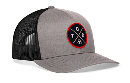 gray-black trucker hat viewed from the right side, showcasing a bold red and black embroidered X patch prominently displayed on the front