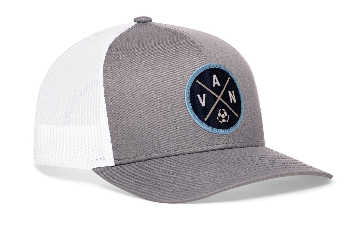gray-white trucker hat viewed from the right side, showcasing a bold blue and white embroidered X patch prominently displayed on the front