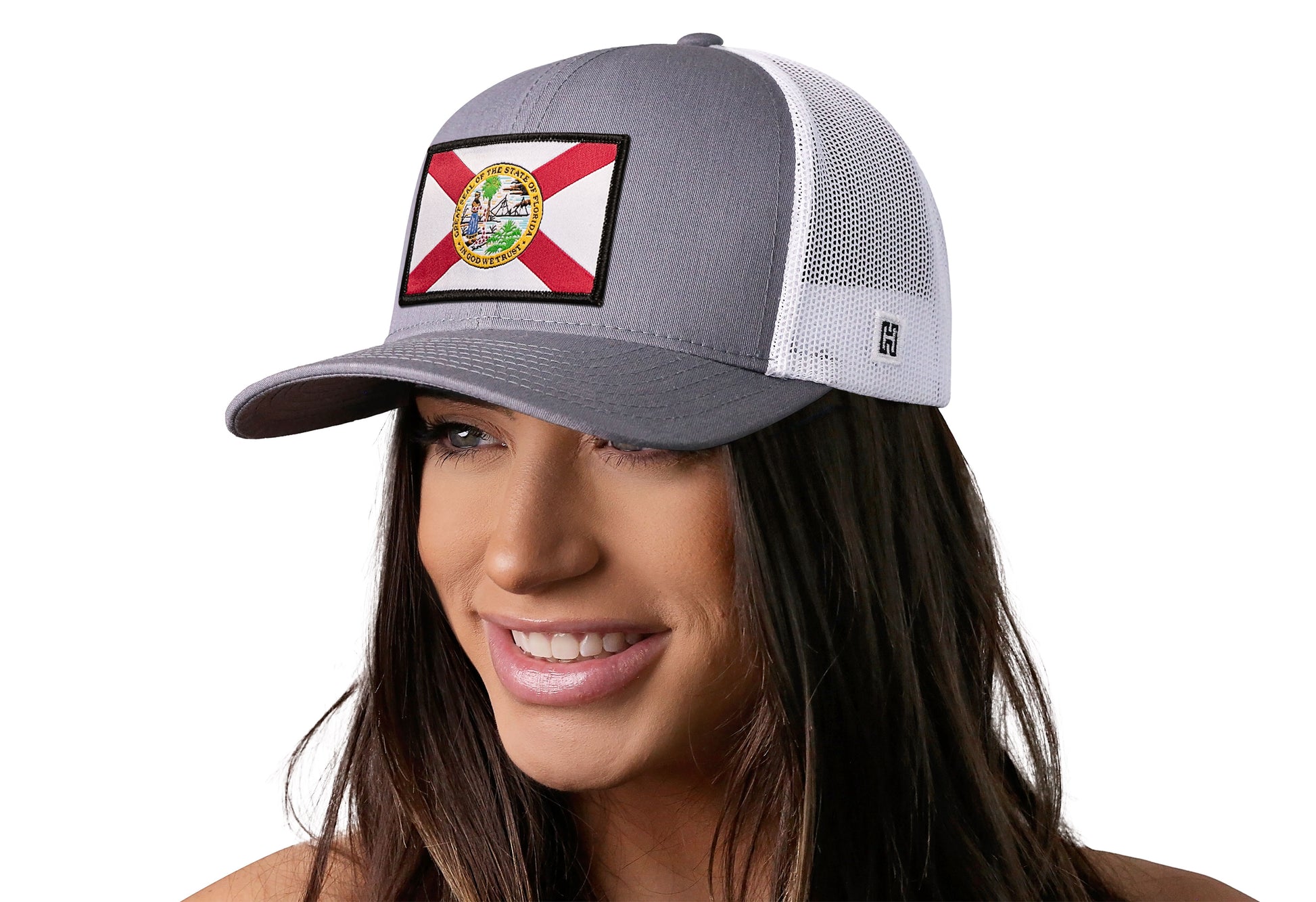 Gray-White trucker hat worn by a female model viewed from the left side and features a Florida Flag Woven Retangle Patch displayed on the front panel. The hat has a classic mesh back design and a curved structured bill