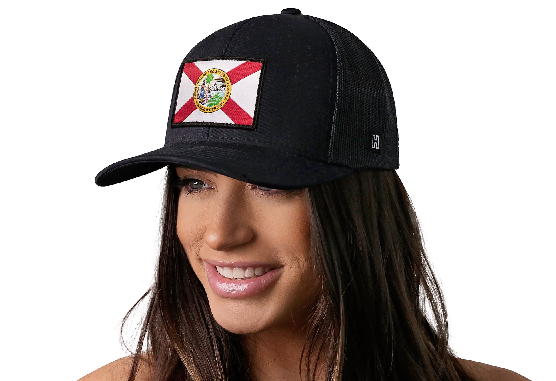 Black trucker hat worn by a female model viewed from the left side and features a Florida Flag Woven Retangle Patch displayed on the front panel. The hat has a classic mesh back design and a curved structured bill