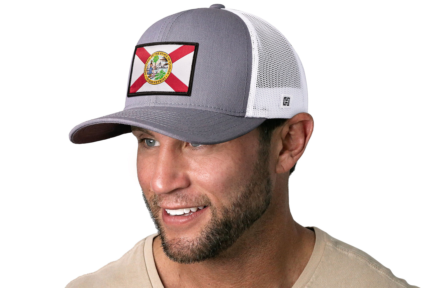 Gray-White trucker hat worn by a male model viewed from the left side and features a Florida Flag Woven Retangle Patch displayed on the front panel. The hat has a classic mesh back design and a curved structured bill