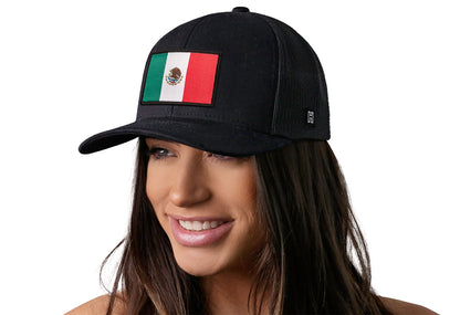 Black trucker hat worn by a female model viewed from the left side and features a Mexican Flag Woven Rectangle Patch displayed on the front panel. The hat has a classic mesh back design and a curved structured bill