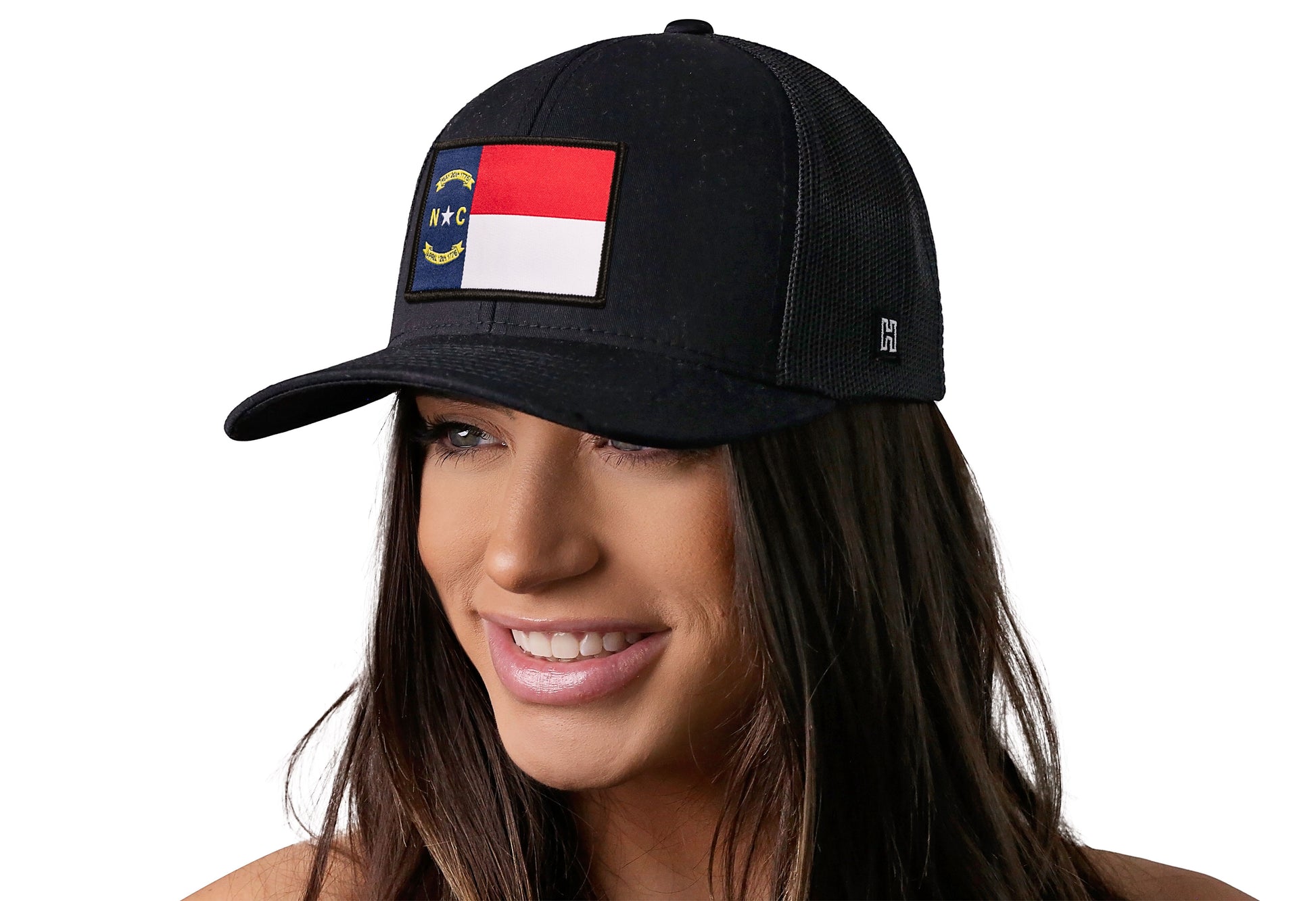 Black trucker hat worn by a female model viewed from the left side and features a North Carolina Flag Woven Rectangle Patch displayed on the front panel. The hat has a classic mesh back design and a curved structured bill