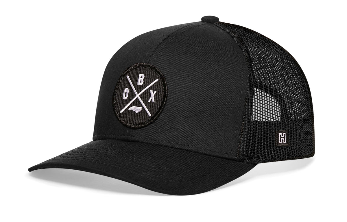 Outer Banks Trucker Hat, black snapback showing Haka brandmark on left side of cap.