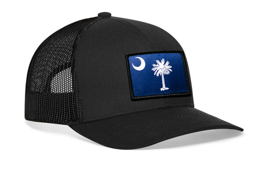 Black trucker hat viewed from the right side, showcasing a South Carolina Embroidered Flag Patch prominently displayed on the front