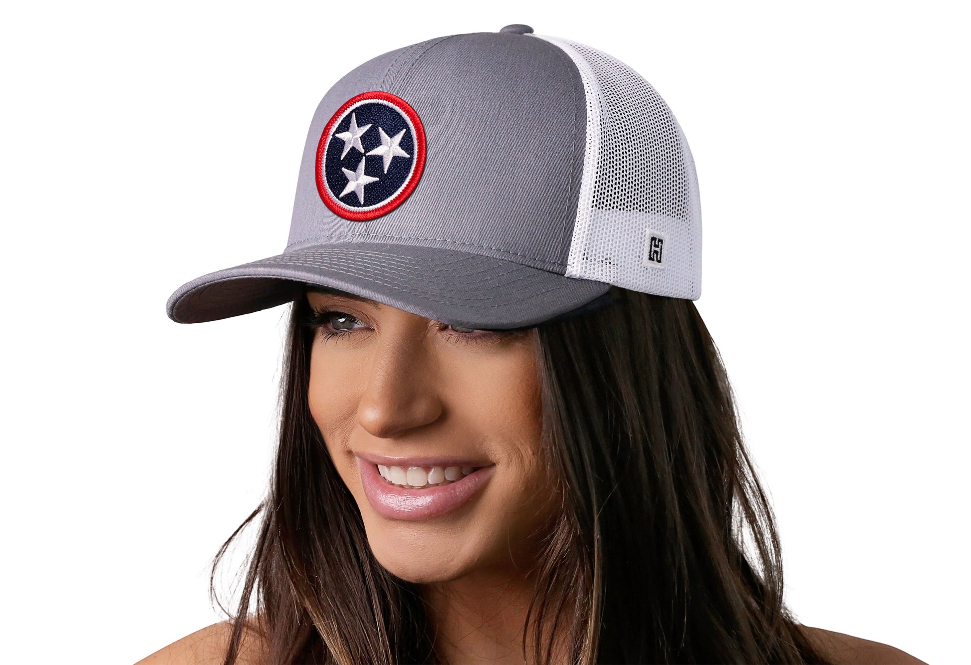 Gray-White trucker hat worn by a female model viewed from the left side and features a Tennessee Embroidered Flag Patch displayed on the front panel. The hat has a classic mesh back design and a curved structured bill