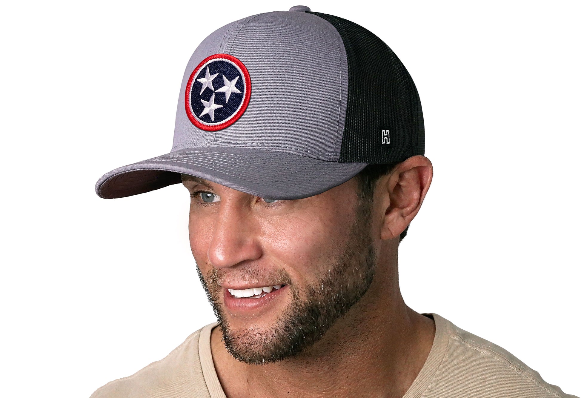 Gray-Black trucker hat worn by a male model viewed from the left side and features a Tennessee Gray- TN Embroidered Flag Patch displayed on the front panel. The hat has a classic mesh back design and a curved structured bill